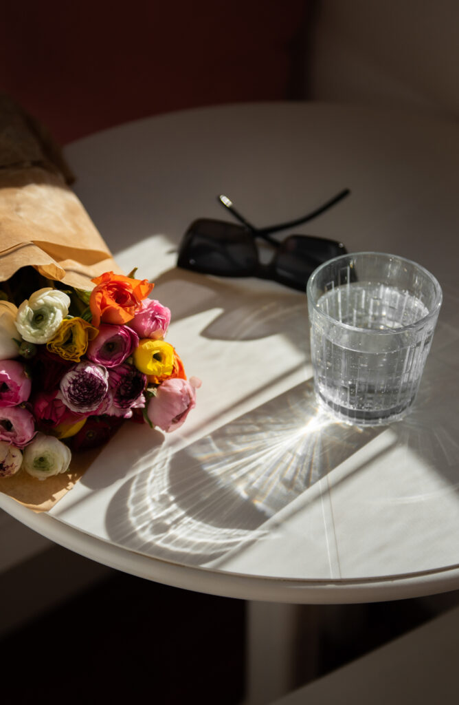 colorful bouquet of flowers on a table with a pair of sunglasses and a glass of water 